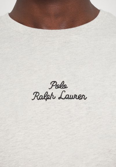 Svetlo siva bombažna majica z okrolim izrezom in črnim vezenim logotipom v pisavi na sprednji strani, na katerem piše "Polo Ralph Lauren".