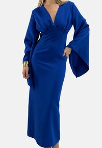 Sukienka w kolorze królewskiego błękitu wykonana z satyny, z głębokim dekoltem w kształcie litery V, długimi, rozszerzanymi rękawami oraz dopasowaną sylwetką, zdobiona marszczeniami na wysokości biustu.