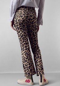 Kalhoty s leopardím potiskem v béžové a černé barvě s přiléhavým střihem, lehce rozšířujícími se u kotníků, doplněné béžovými vysokými teniskami.