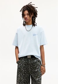 Lyseblå oversized t-shirt med et diskret logo, parret med grå leopardprint bukser, der har et sort bælte og sølvfarvede kædeaccessories.