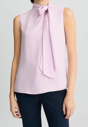 Mouwloze lichtpaarse blouse met een hoge halslijn en een gestrikte strik, gecombineerd met donkerblauwe broek, getoond op een staand persoon.