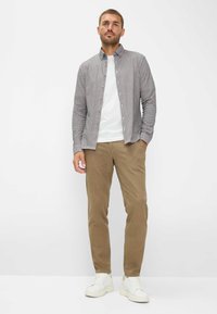 Camicia a quadri blu e bianca, abbinata a una t-shirt bianca semplice, pantaloni beige e sneakers bianche su uno sfondo neutro.