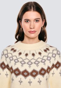 Sweter w kolorze kremowym z okrągłym dekoltem, zdobiony wzorem w diamenty i geometrycznym w odcieniach brązu, szarości i różu. Miękka tekstura dzianiny.
