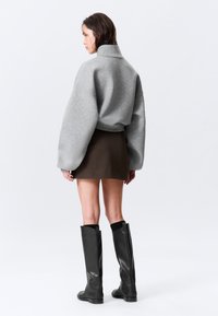 Sudadera gris recortada con mangas extragrandes, combinada con una falda ajustada marrón de canalé y botas negras hasta la rodilla. Diseño minimalista en general.