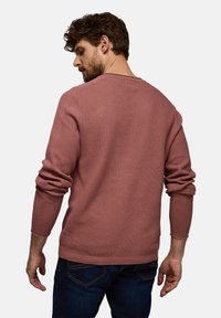 Waffelstrick-Pullover mit langen Ärmeln in staubigem Rosa, mit Rundhalsausschnitt und gerippten Bündchen, kombiniert mit dunklen Jeans.