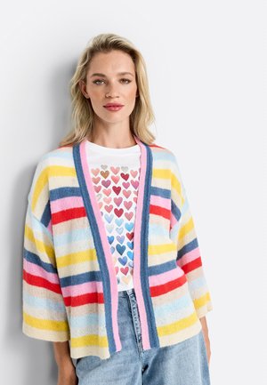 Cardigan rayé en tissu doux, présentant des teintes jaunes, bleues, roses et rouges, avec une fermeture ouverte et des épaules tombantes sur une chemise à motifs de cœurs.