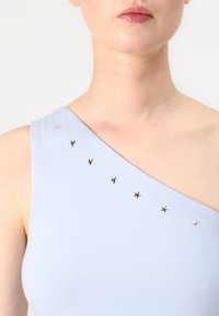 Svetlomodrý top bez rukávov s asymetrickým dizajnom; zdobený malými striebornými hviezdičkami pozdĺž ramena. Mäkka textura.