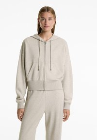Light gray zip-up hoodie made of soft fabric, featuring a front pocket, drawstring hood, and ribbed hem and cuffs.