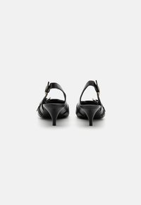 Sandálias de salto alto em couro preto com costas abertas, salto alto esguio e uma fivela decorativa na tira do tornozelo. Textura suave, design minimalista.