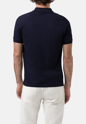 Polo bleu marine à manches courtes, col classique, lignes épurées et texture en coton lisse. Porté avec un pantalon de couleur claire, sans motifs.