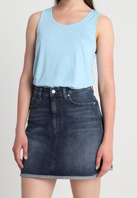 Ljusblå linne av mjukt tyg, kombinerad med en mörk denim a-linje kjol med rå kant och fem bältesöglor.