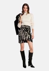 Jupe rayée noir et blanc avec un design en portefeuille, associée à un pull à col roulé crème et des bottes noires jusqu'aux genoux. Inclut un blazer noir drapé par-dessus.