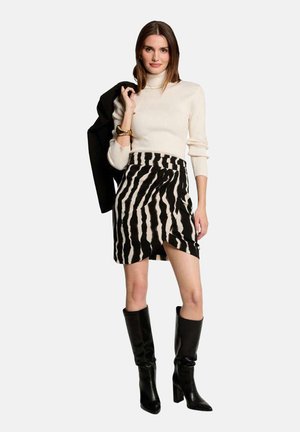 Jupe rayée noir et blanc avec un design en portefeuille, associée à un pull à col roulé crème et des bottes noires jusqu'aux genoux. Inclut un blazer noir drapé par-dessus.