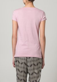 Camiseta corta de manga corta en rosa claro, con escote redondo y una textura suave. Combinada con pantalones estampados en blanco y negro.