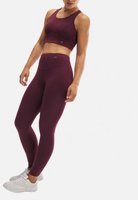 Sujeción deportiva burdeos y leggings de talle alto, fabricados con tejido suave. Presenta un diseño ajustado y una sutil marca en la cintura.