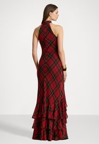 Rochie în carouri roșii cu un design cu gât halter, volane stratificate la margine și accente verzi și galbene în model. Material neted și fluid.