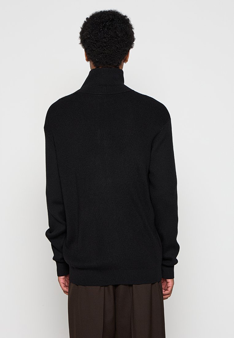 Übergrößener schwarzer Strickpullover mit hohem Kragen und geripptem Muster, ausgestattet mit langen Ärmeln und einer lockeren Passform.