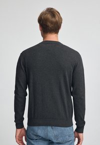 Mörkgrå tröja i mjukt tyg, med långa ärmar, rundad halsringning och ribbade ärmslut och nederkant. Enkel, figursydd design.