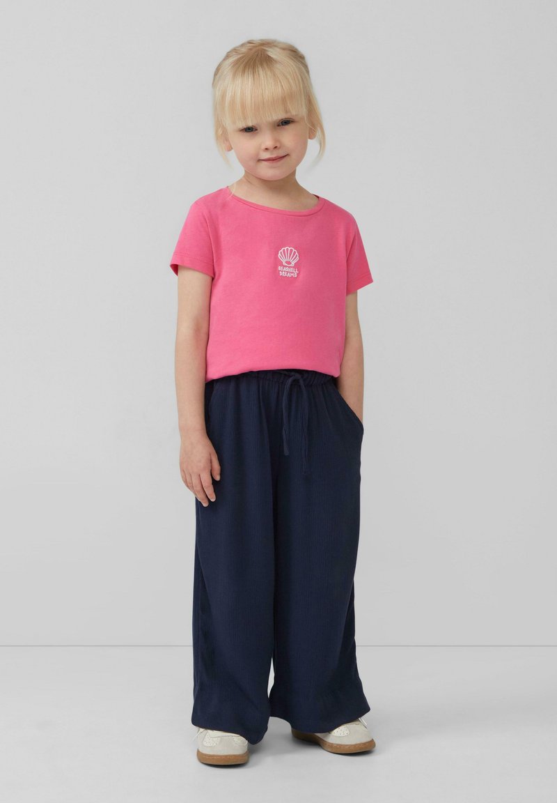 Rosa T-Shirt mit kurzen Ärmeln und Muschelgrafik, kombiniert mit lockeren navyblauen Hosen. Das Outfit hat einen Kordelzug in der Taille und besteht aus leichtem Stoff.