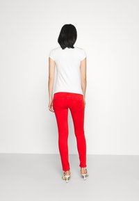Chemise blanche à manches courtes associée à un jean rouge ajusté. Le jean comporte des poches arrière et une texture lisse, tandis que la chemise est simple et unie.