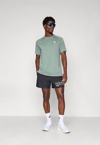 Heleroheline lühikeste varrukatega sportlik särk logoga, mustad lühikesed püksid valge kirjaga, valged tossud ja spordiprillid.