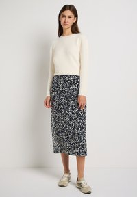 Cremfarbener, flauschiger Pullover mit langen Ärmeln; marineblaue Midirock mit floralem Muster; Model trägt beige Sneakers mit dunklen Akzenten.
