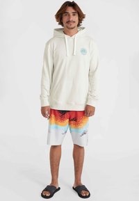 Cream hoodie with front pouch pocket and turquoise logo; bright multicolored swim shorts with gradient pattern; black flip-flops.