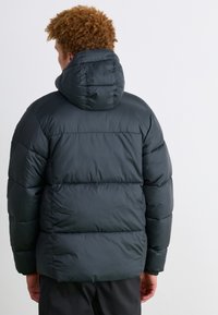 Schwarze Daunenjacke mit Kapuze, ausgestattet mit einem gesteppten Design und elastischen Bündchen. Weiche, glänzende Textur und eine lockere Passform für optimale Isolierung.