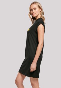 Schwarzes kurzärmliges Kleid aus Baumwolle mit lockerer Passform, das einen schlichten runden Halsausschnitt und einen gelben grafischen Akzent auf der Brust aufweist.