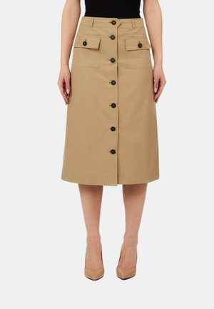 Gonna beige fino al ginocchio con bottoni neri frontali e due tasche con patta, indossata con tacchi beige e una maglia nera, mostrata dalla metà coscia in giù.