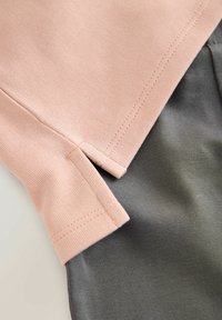 Svetloružová látka s textúrovaným povrchom prekrytá tmavosivou bavlnou, ktoré vystavujú čisté švy a bočné rozparky pre lepšiu pohyblivosť.