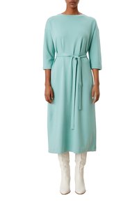 Un lungo vestito verde menta realizzato in tessuto morbido, con maniche a tre quarti, una cintura legata in vita e una vestibilità comoda. Indossato con stivali bianchi.