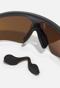 Lunettes de sport avec une monture noire et des verres marron. Comprend un support de nez noir avec des détails de grip texturé.