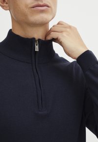 Navy Zip-Jacke mit geripptem Kragen und Bündchen, ausgestattet mit einem halben Reißverschluss und glatter Textur. Nahaufnahme des Halsausschnitts und des Stoffes.