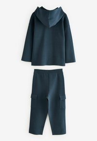Dunkelblauer Baumwoll-Hoodie mit Kapuze und langen Ärmeln, kombiniert mit passenden, hochgeschnittenen Hosen, die auf jeder Seite zwei Cargo-Taschen haben.