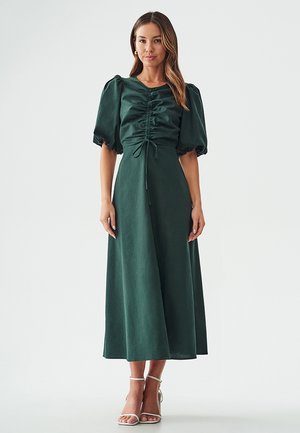 Green, knee-length dress with puffed sleeves and a scrunched bodice. Made of smooth fabric; cinched waist accentuated by tie detail.