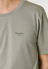 Light gray-green short sleeve T-shirt with small dark green "Pepe Jeans London" logo on the left chest.