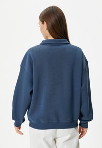 Sudadera de gran tamaño en color azul marino con cuello doblado, hombros caídos y puños y dobladillo acanalados; textura suave y corte relajado.