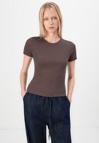 Rjava rebrasta kratka majica s krojem okroglega izreza, v kombinaciji s prostornimi modrimi denim hlačami, ki imajo elastičen pas in žepke.
