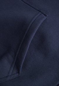 Marinblått tyg i närbild med en texturerad väv. Har en vikt fickdetalj och ren sömnad längs kanterna.