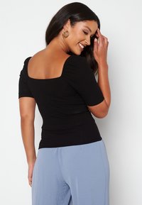 Sort ribbet top med firkantet U-hals, korte pufærmer og tætsiddende design. Kombinationen med lyseblå bukser, der viser en glat tekstur.