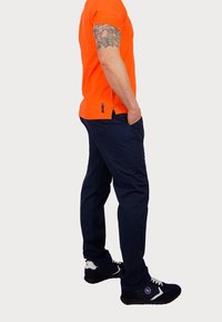 Orange short-sleeve t-shirt paired with dark blue pants and black sneakers. The outfit features a fitted design and subtle detailing.