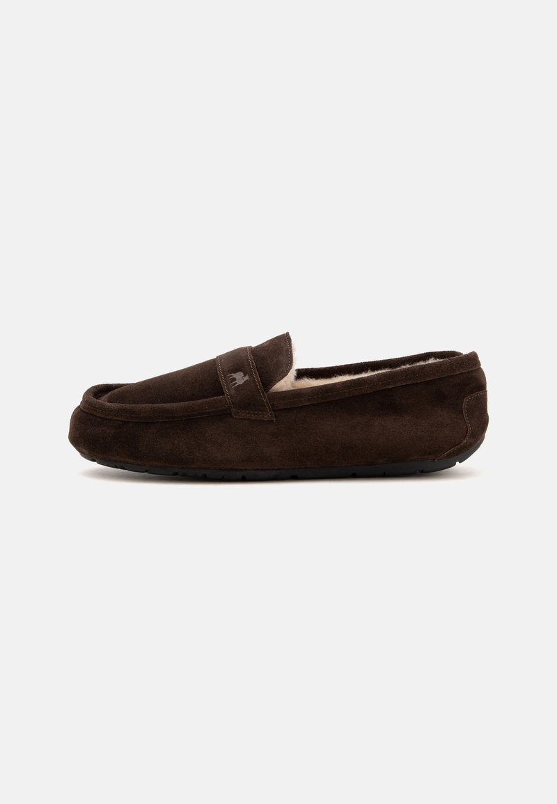 Chausson mocassin en daim marron avec une doublure intérieure douce et une semelle en caoutchouc, présenté de côté sur un fond uni.