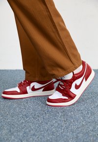 Rode en witte Nike-sneakers met leren en synthetische materialen, een lage hak, platte witte veters en rode accenten.