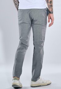 Graue, schlanke Hosen mit einem strukturierten Stoff, ausgestattet mit Gesäßtaschen und einem mittelhohen Bund, getragen mit weißen Sneakers.