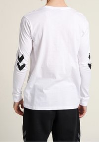 Witte katoenen t-shirt met lange mouwen en een ronde halslijn, voorzien van zwarte chevronpatronen op de mouwen en een rechte zoom bij de taille.