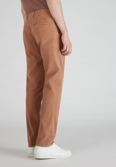 Brązowe bawełniane spodnie o prostym kroju nogawki, z tylnymi kieszeniami i przeszyciami, w połączeniu z białymi sneakersami.