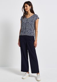 Top blu navy a fantasia con maniche corte, abbinato a pantaloni larghi blu navy e sneakers bianche. La trama del tessuto è leggera e liscia.