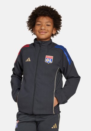 Zwarte sportjack met blauwe en rode gestreepte schouders, gouden accenten, ritssluiting en het logo van Olympique Lyonnais. Gladde textuur.