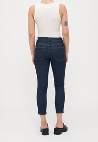 Jean skinny bleu foncé taille haute, cinq poches, avec une texture denim lisse. L'ourlet se termine à la cheville.